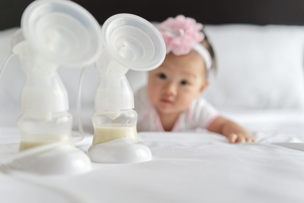 Breast milk in milk pump's bottles on the bed with little cute baby crawling in background