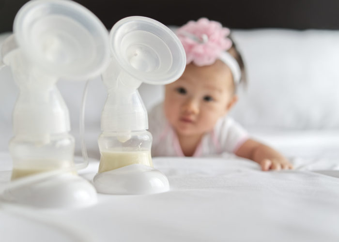 Breast milk in milk pump's bottles on the bed with little cute baby crawling in background