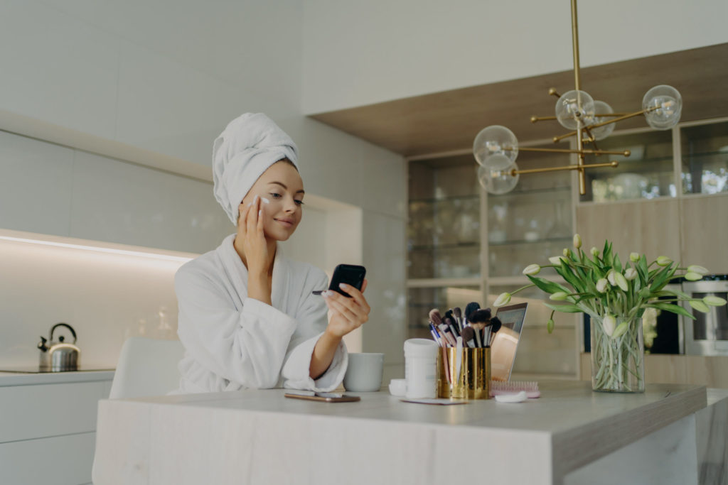 Happy healthy woman in bathrobe doing skincare daily routine after taking shower or bath at home