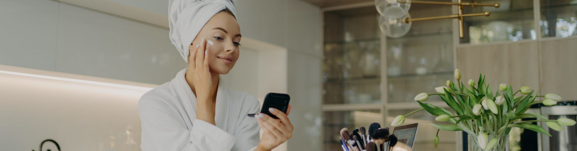 Happy healthy woman in bathrobe doing skincare daily routine after taking shower or bath at home