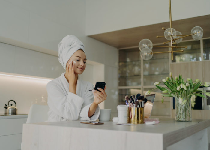 Happy healthy woman in bathrobe doing skincare daily routine after taking shower or bath at home